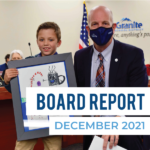 Superintendent Nye stands with card contest winner. Text: Board Report December 2021